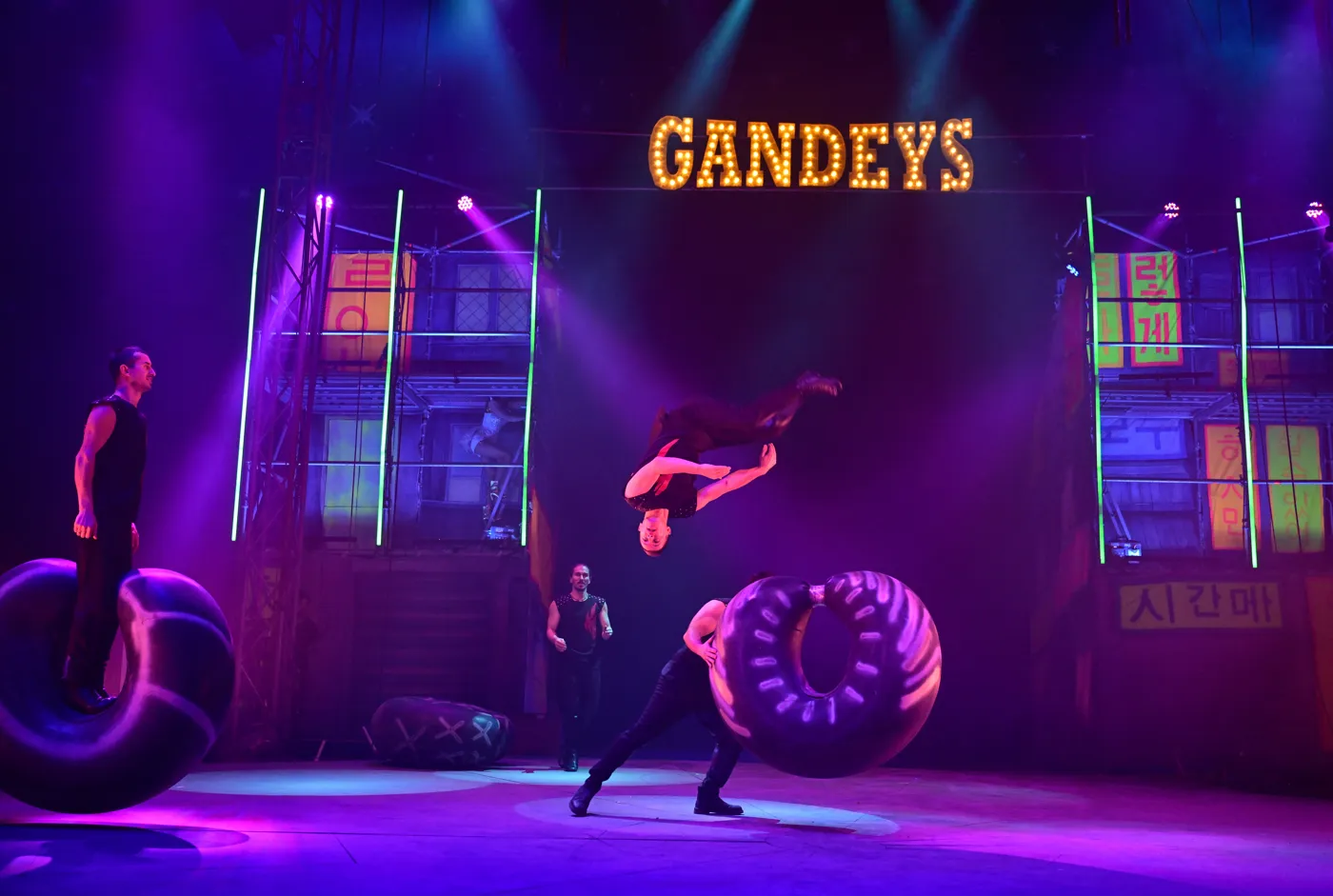 An acrobat somersaults between two giant inflatable rings on a purple-lit stage