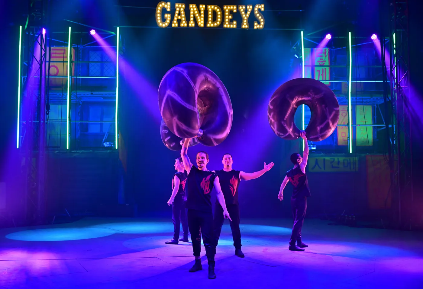 Four acrobats balancing giant inflatable rings on a blue-lit stage
