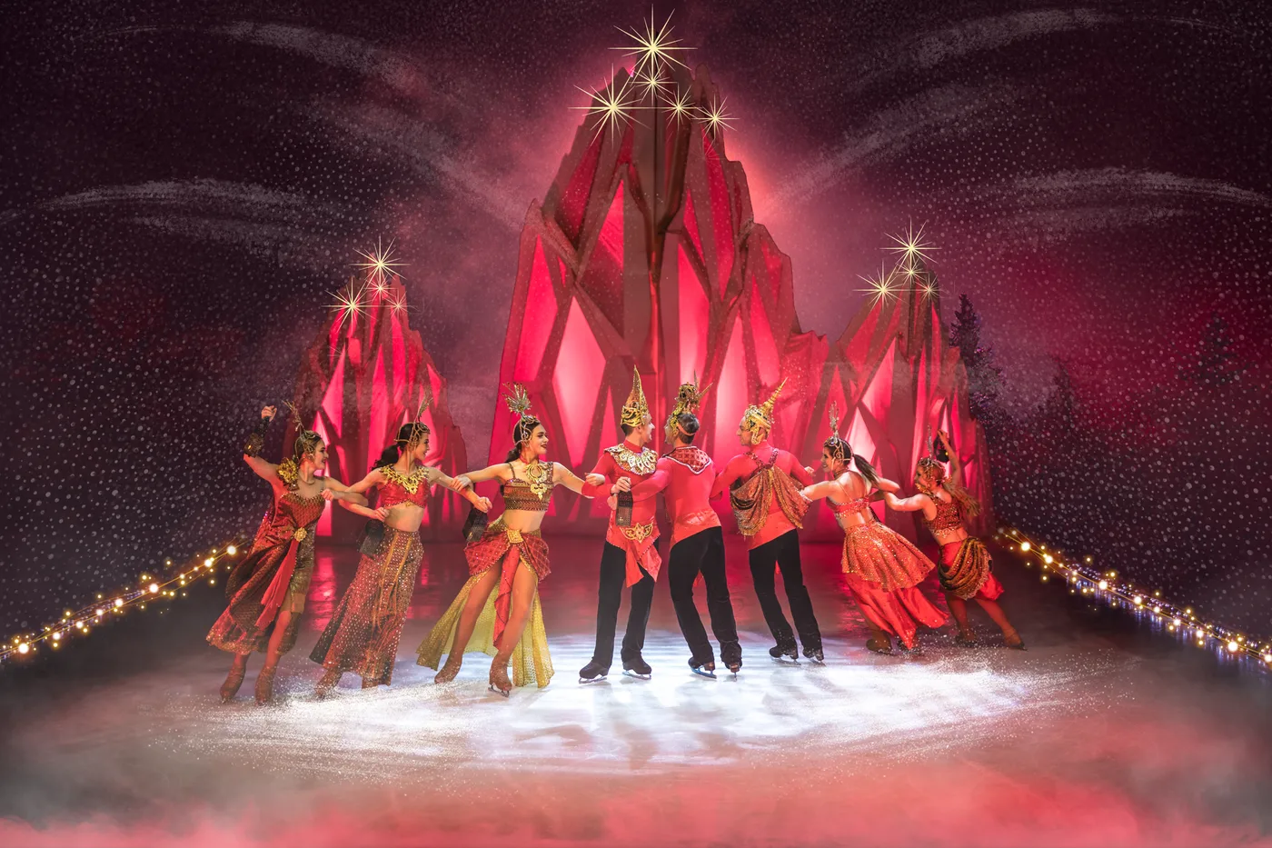 Skaters in red and gold costumes in front of a red-lit ice castle set