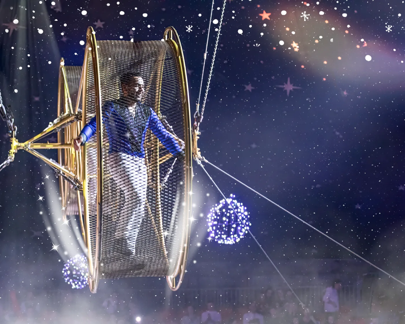 A performer in a blue jacket stands inside a large gold wheel hung above the rink